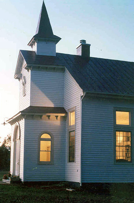 A grainy color photograph of a country church house that has been converted to a private residence.